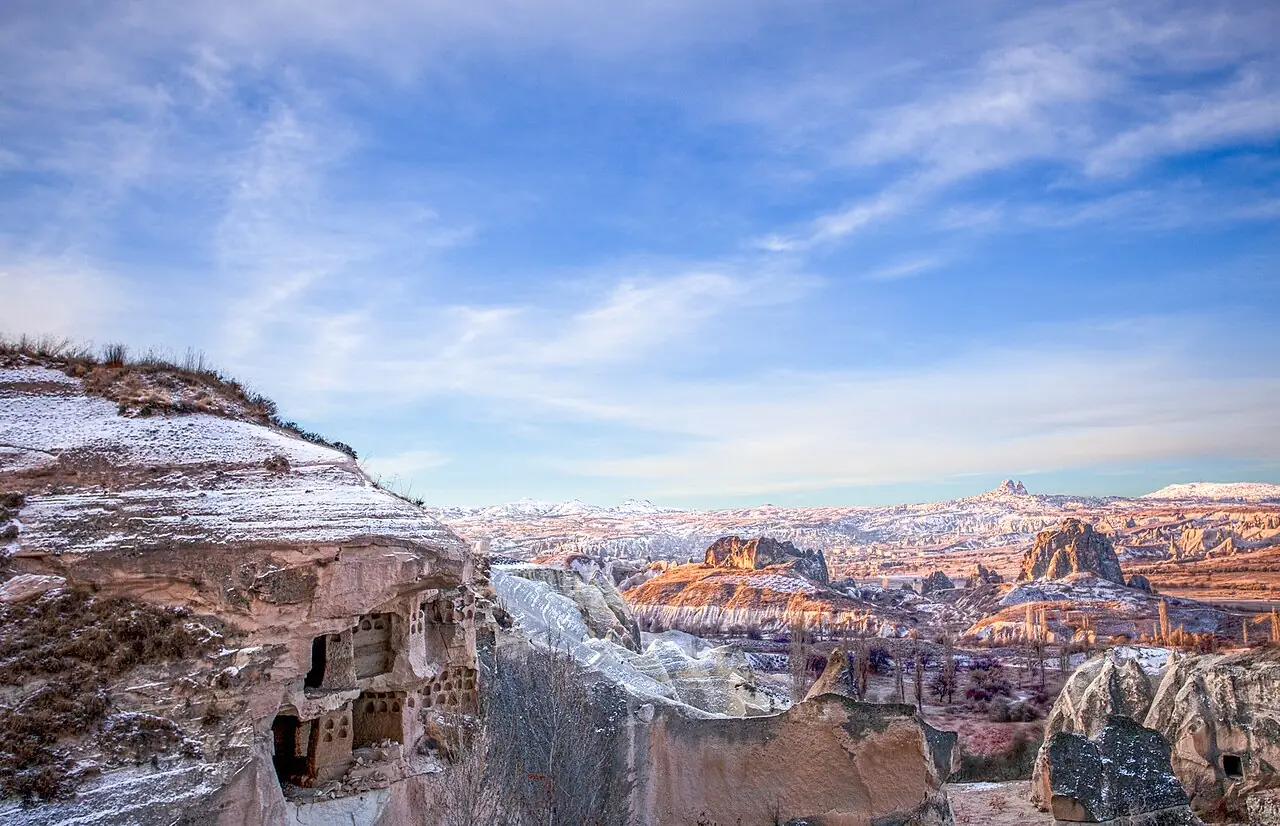 Light snow covers Cappadocia cliffs and cave dwellings beneath a blue winter sky.