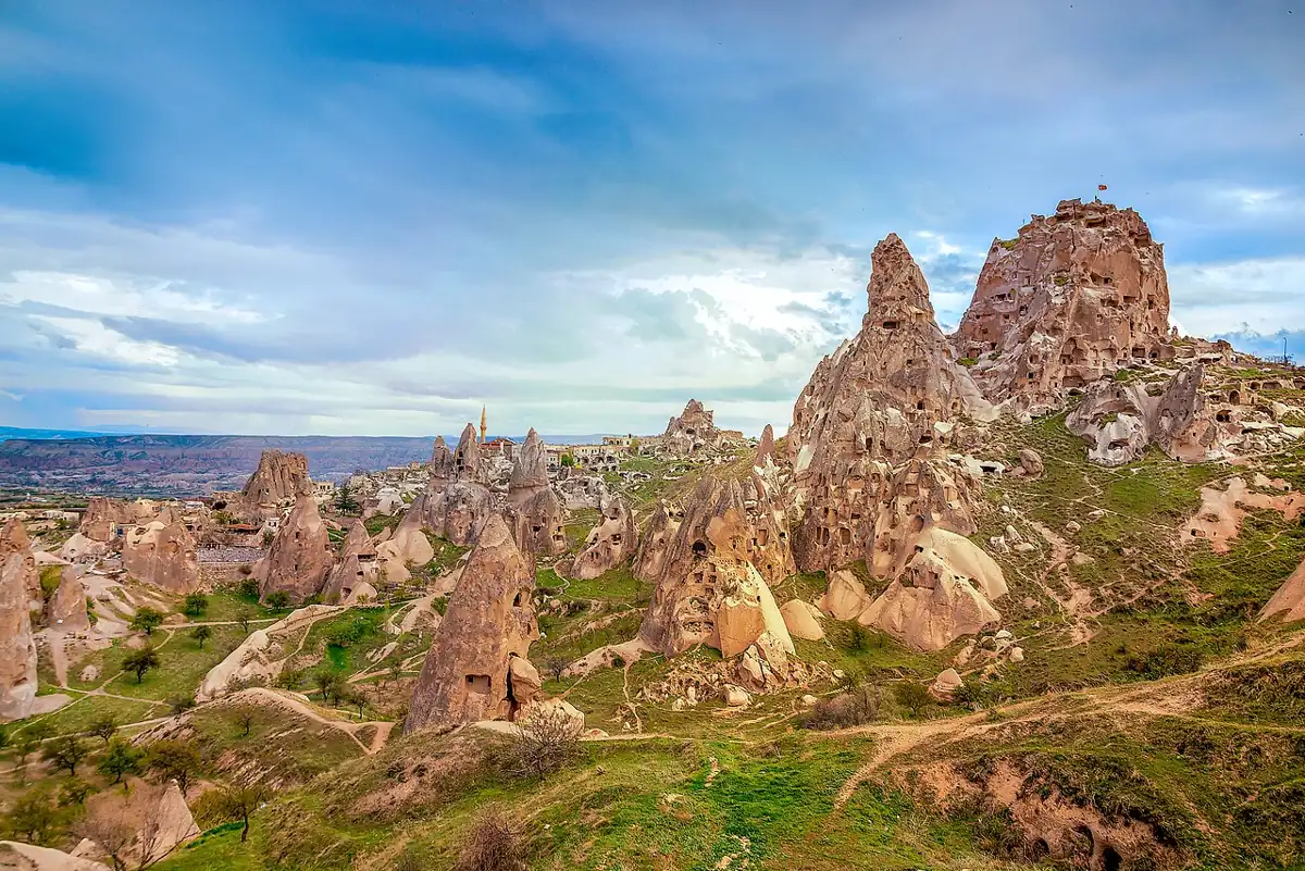 Uçhisar Castle rises above green slopes and fairy chimneys in Cappadocia.