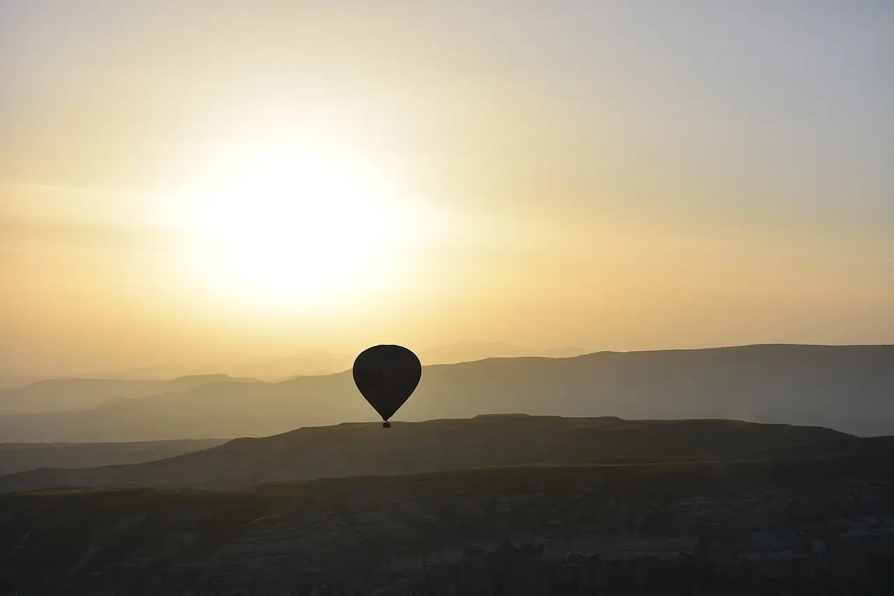 A hot air balloon silhouetted above Cappadocia hills at golden sunrise.